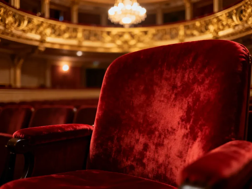 Eleganckie, czerwone krzesło w zabytkowym wnętrzu teatru, podkreślające wyrafinowany klimat wieczornego wyjścia.
