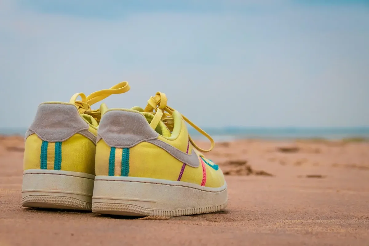 Klasyczne białe sneakersy z czarnymi paskami na minimalistycznym betonowym tle.